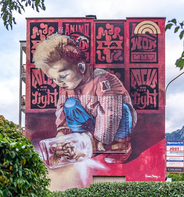 Large red mural of a person crouching and painting, with bold black and pink graffiti-style lettering.