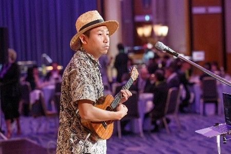 Nao Hiramoto playing ukulele on stage at Hilton Nagoya Oogi Ballroom.