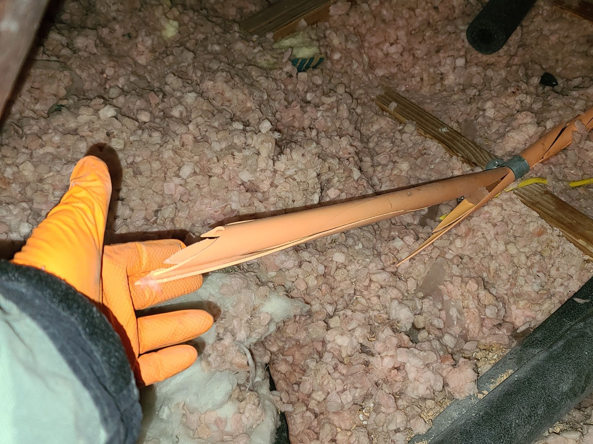 A person wearing orange gloves is holding a piece of insulation in their hand.