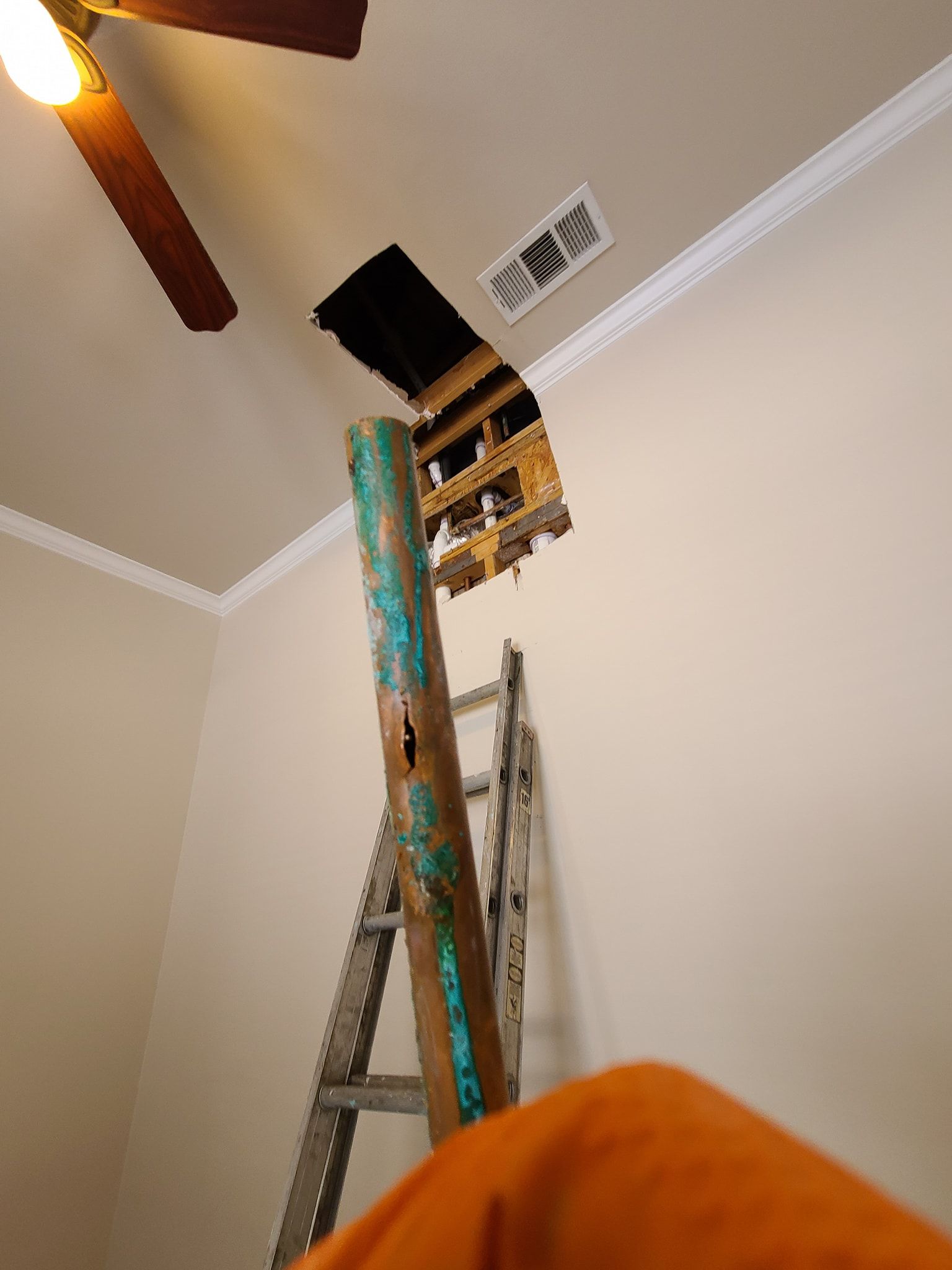 A ladder is sitting in a room next to a hole in the ceiling.
