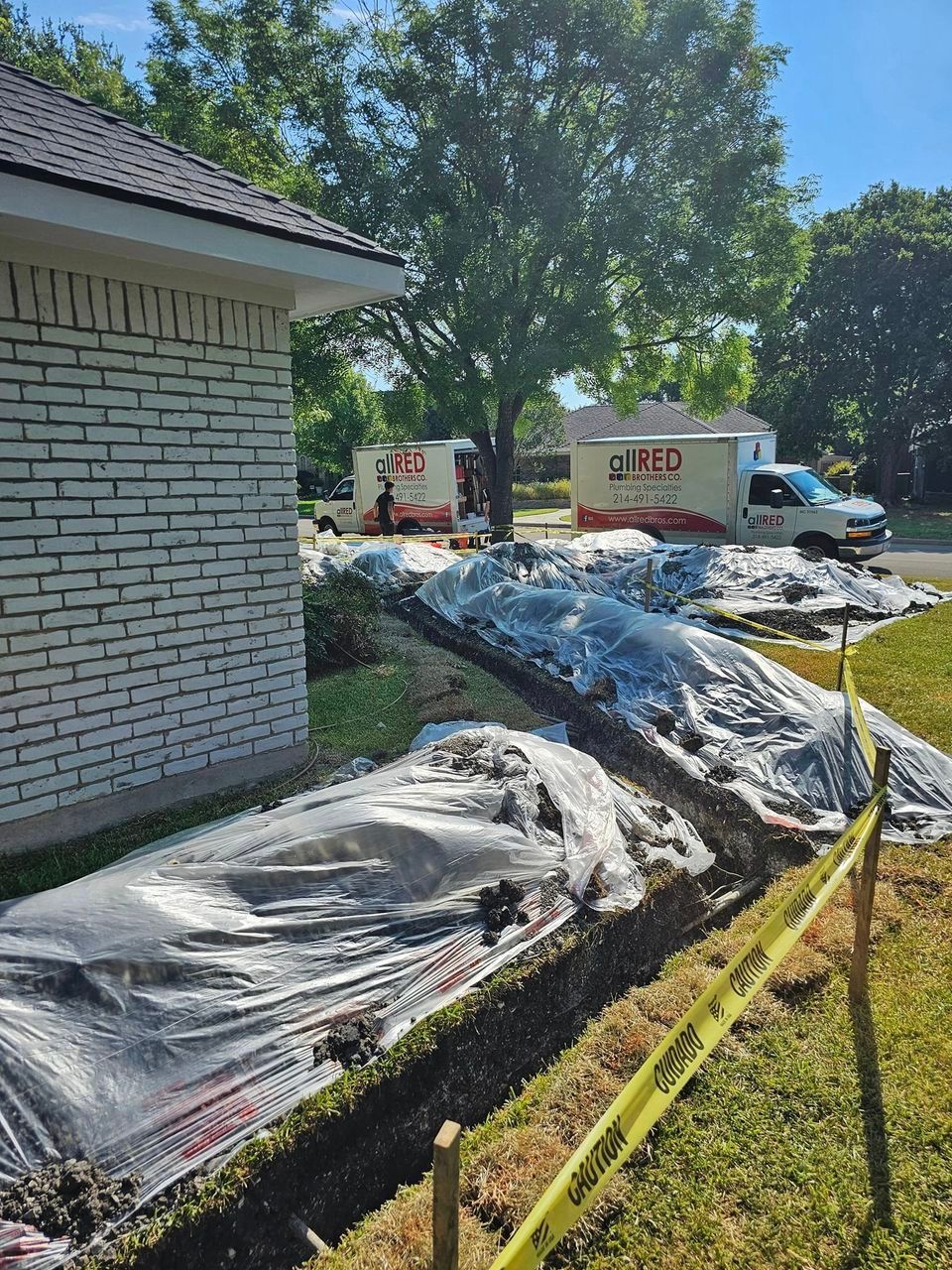 A brick house is having drain work done in the front yard.