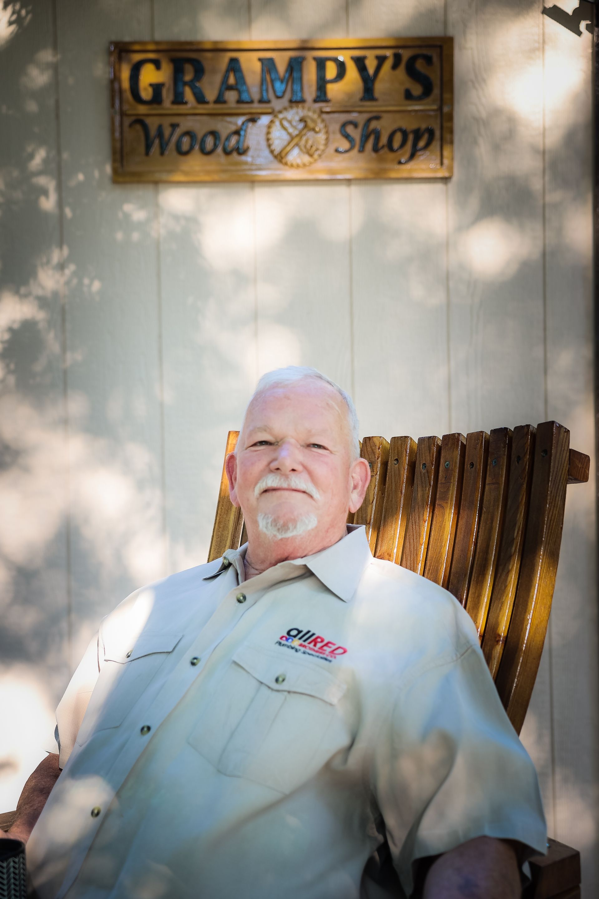 A man is sitting in a chair in front of a sign that says grampy 's wood shop