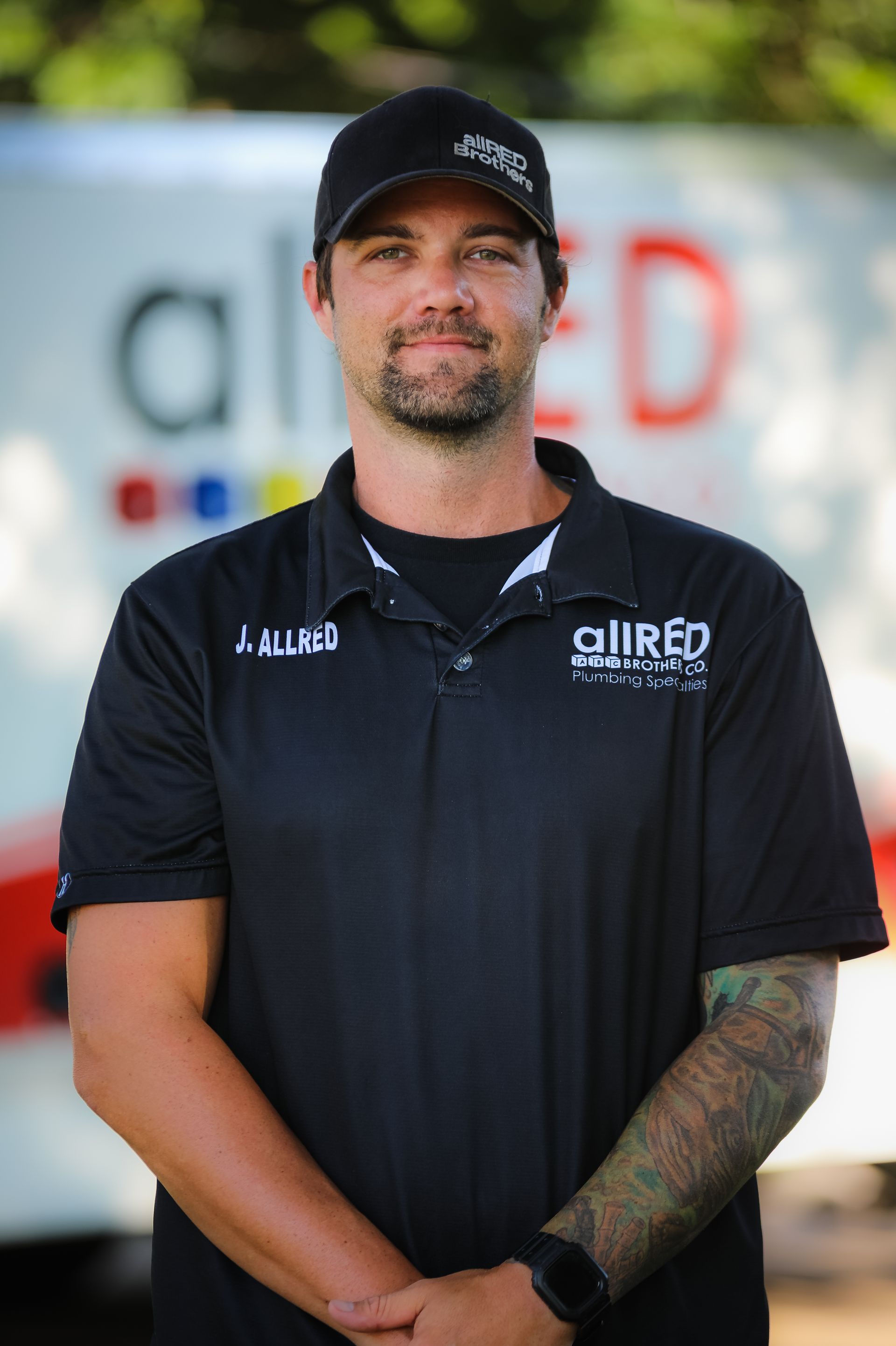 A man in a black shirt and hat is standing in front of a truck.