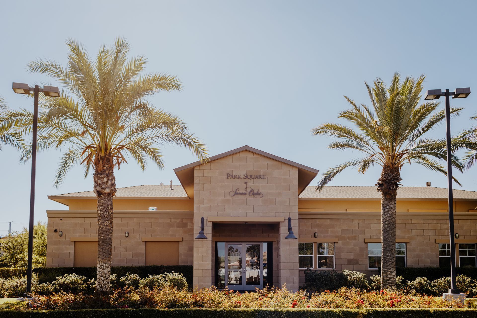 Building exterior with palm trees, beige facade, and sign above entrance. Clear blue sky.