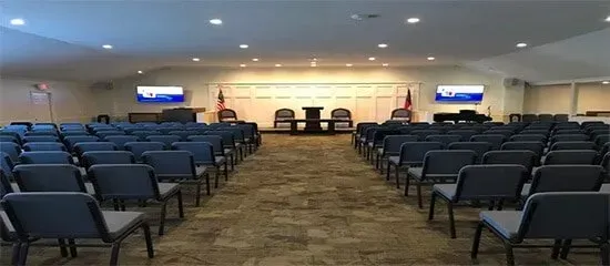 Empty conference room with rows of blue chairs facing a stage and presentation screens