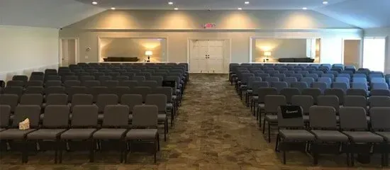 Empty conference room with rows of dark chairs facing a front wall and double doors