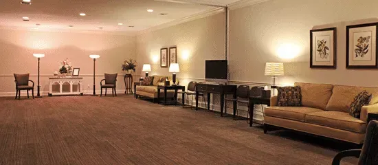 Spacious beige lounge with sofas, lamps, side tables, and framed wall art on a carpeted floor.