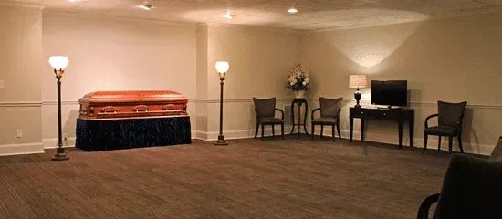 Empty funeral parlor room with a casket on a raised stand, chairs, and lamps along the wall
