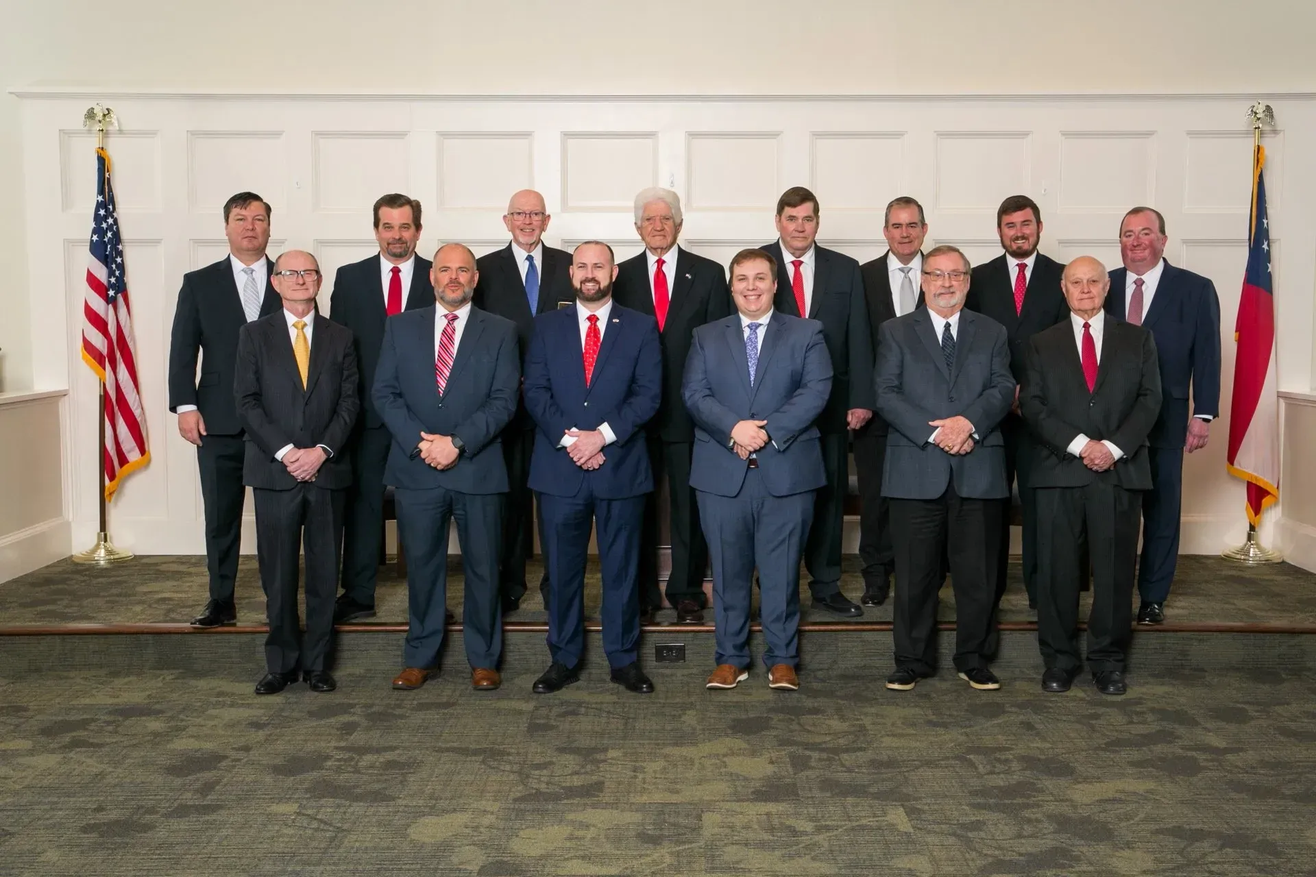 Group of officials in suits posing indoors with U.S. and Texas flags in the background