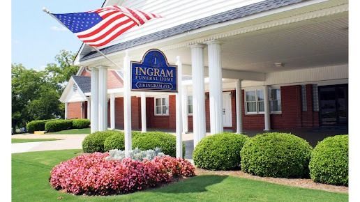 American flag outside Ingram building with white columns, brick facade, and landscaped shrubs