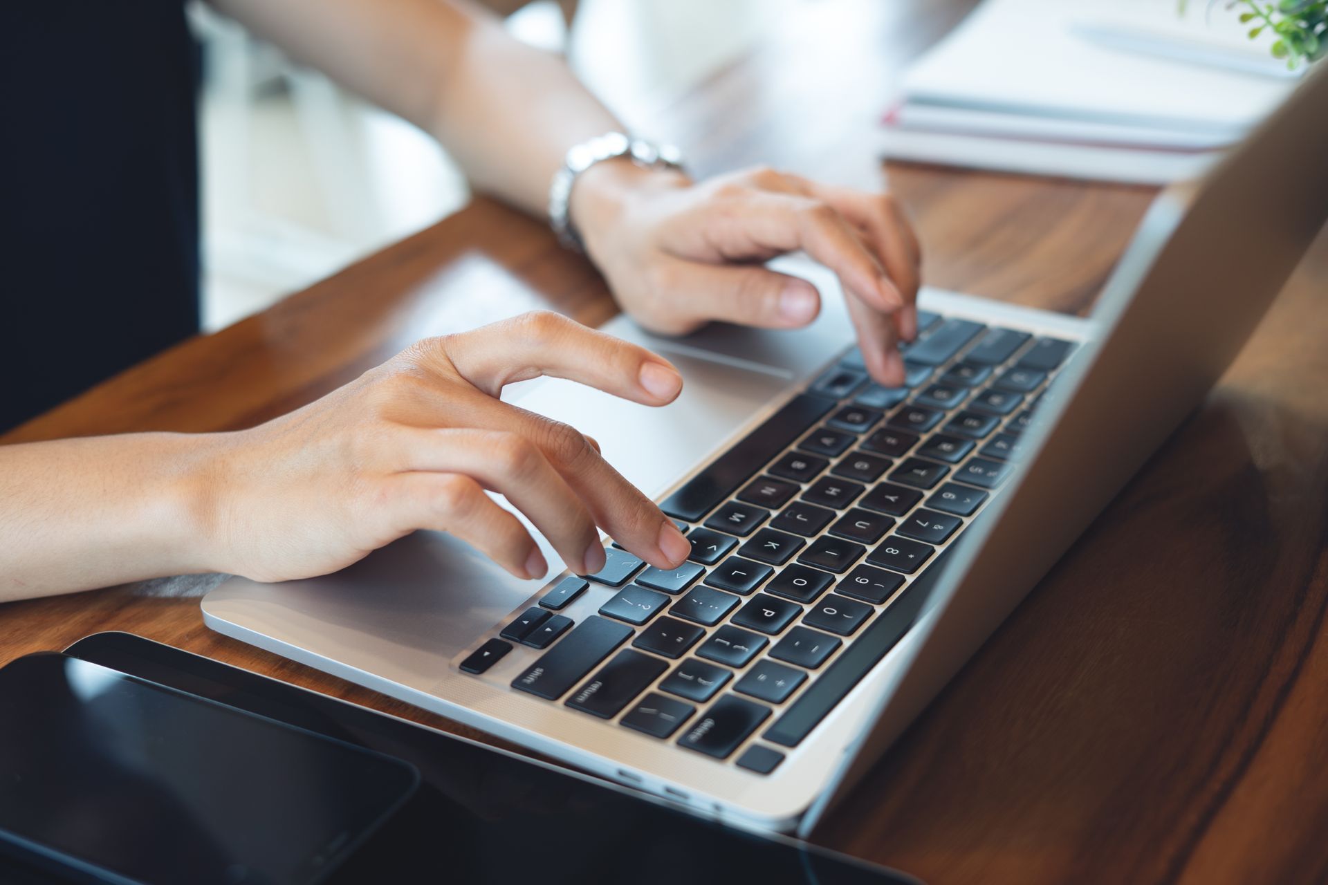 Hands typing on a silver laptop at a wooden table