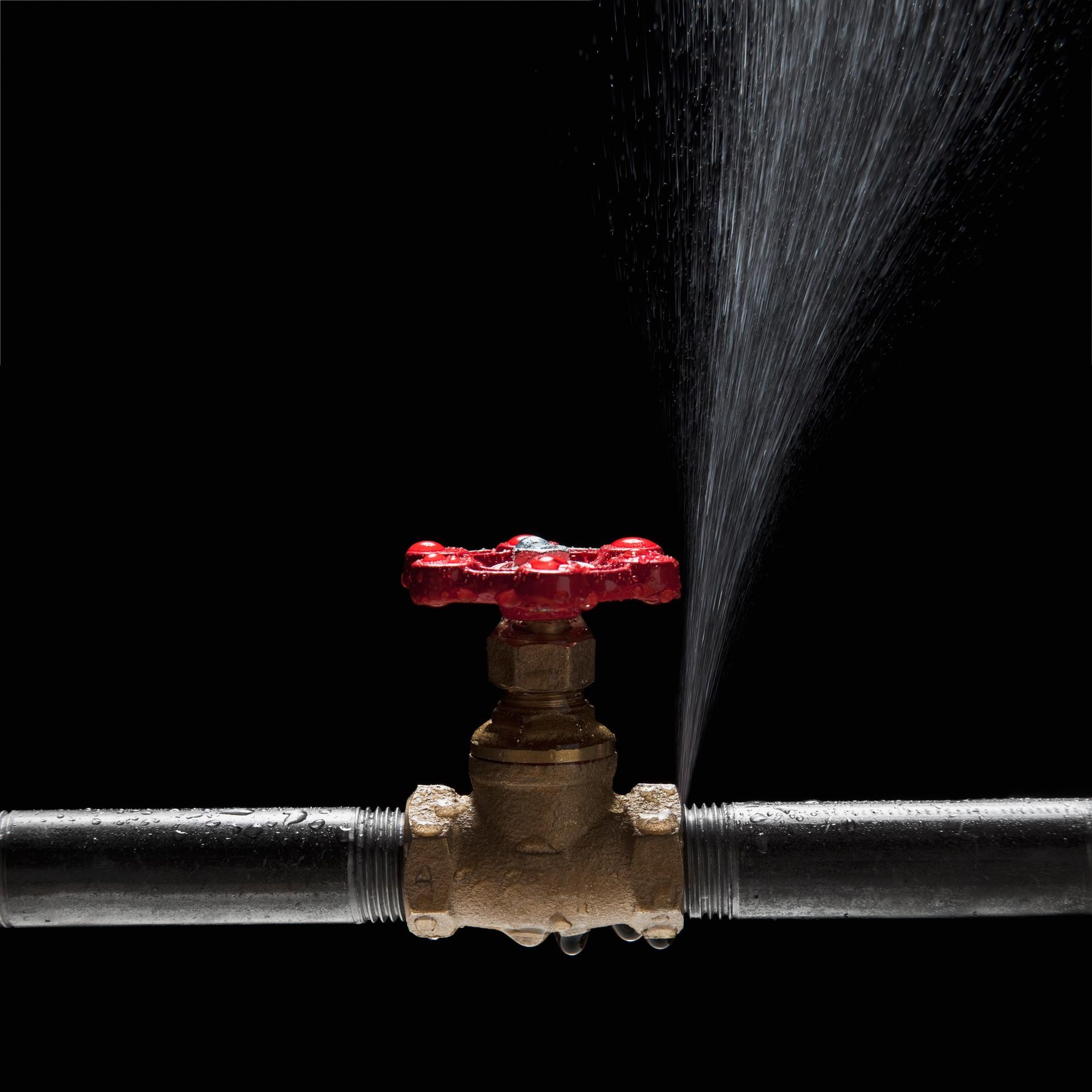 Water spraying from a leaky pipe connected to a red-handled valve, on a black background.