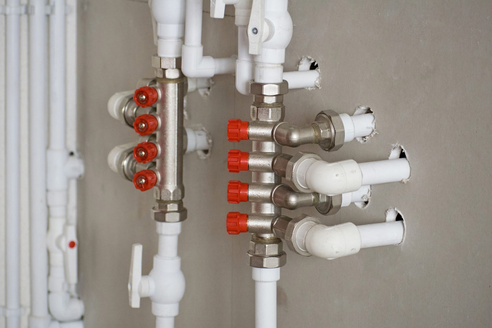 Piping system with white and metal pipes, red valve handles, installed against a gray wall.