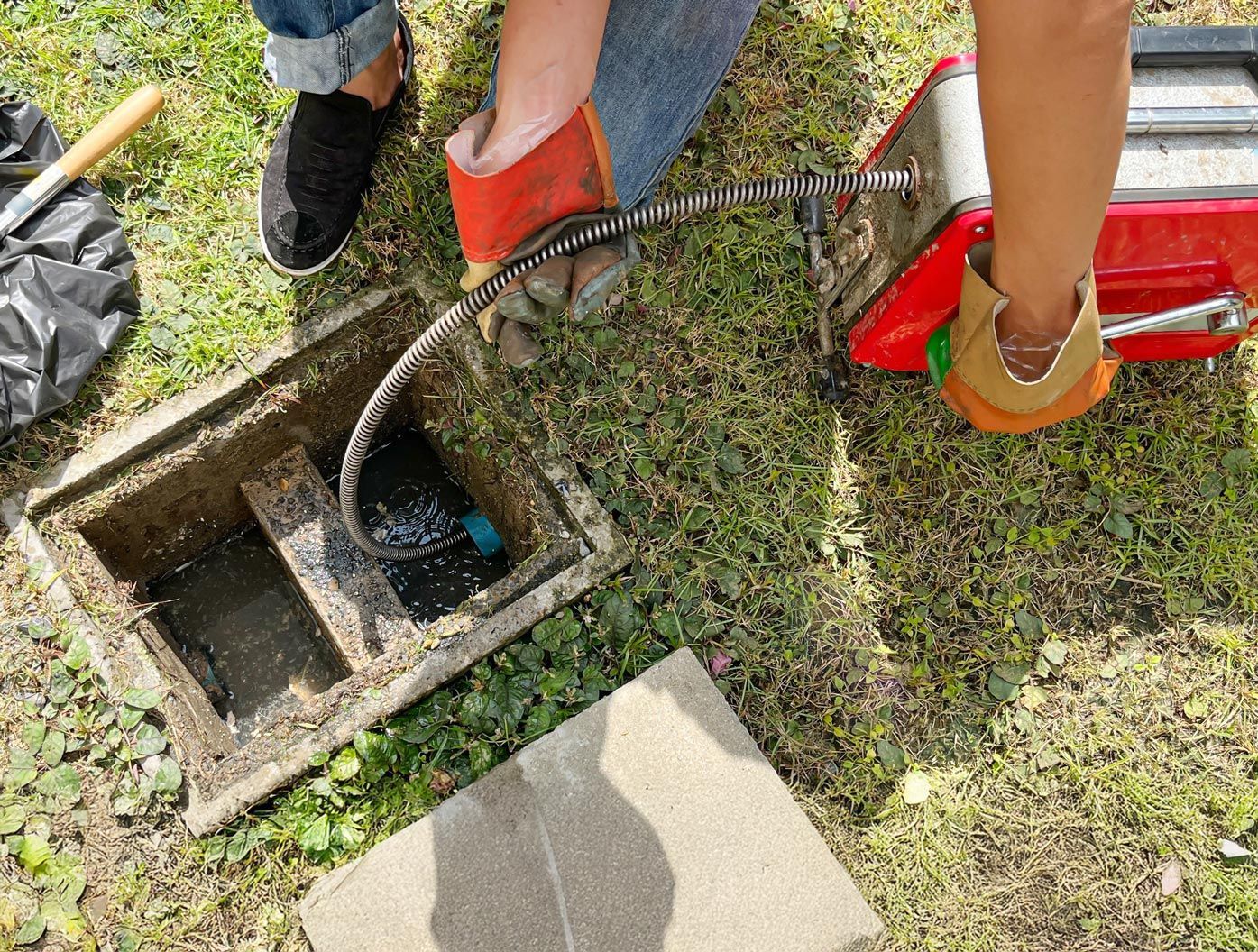Person using a tool to clean out an open concrete box on grassy ground.