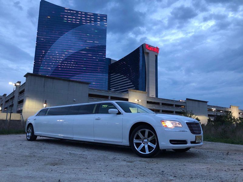 A white limousine is parked in front of a large building.