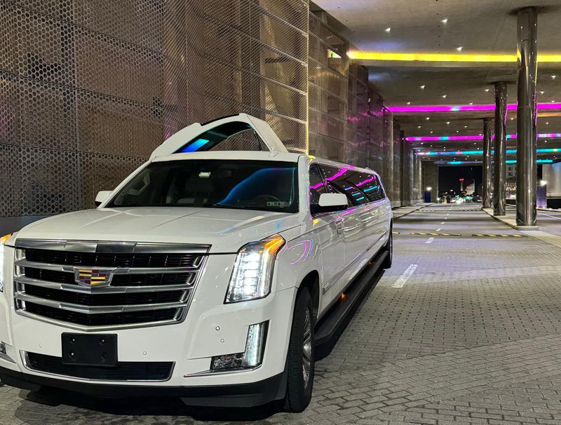 A white cadillac escalade limousine is parked in a parking lot.