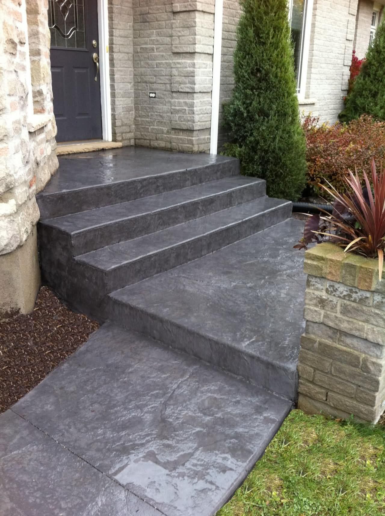 Front entrance with dark gray concrete steps and sloped accessible ramp beside stone and brick walls