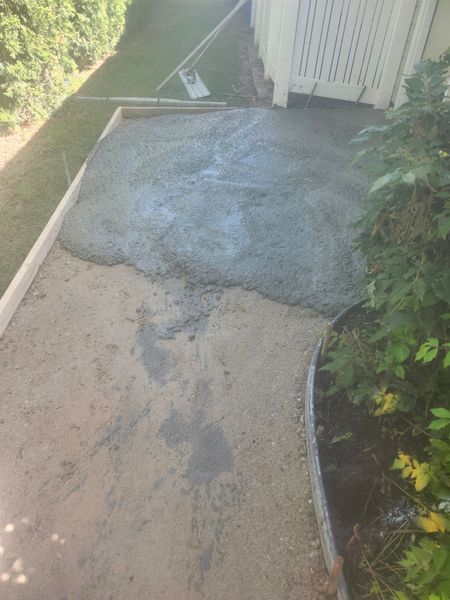 Damaged concrete walkway beside a house, with a patched gray section and grass along the edge