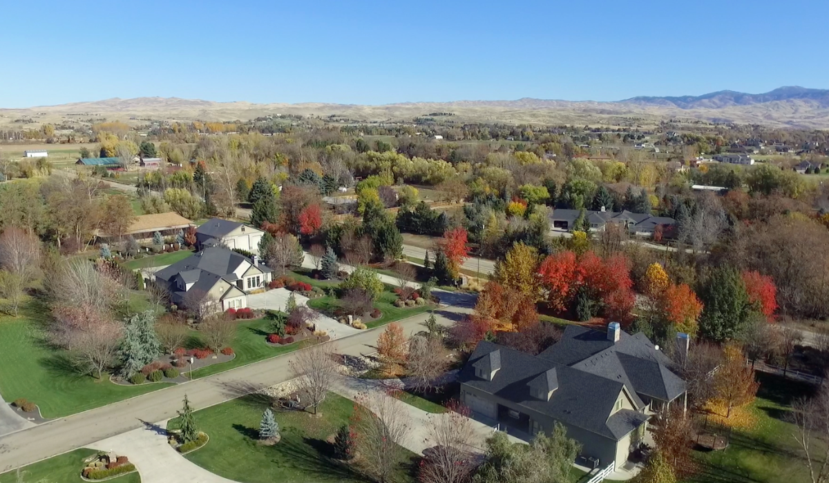Aerial view of a suburban neighborhood with autumn trees, houses, and distant mountains under a clear blue sky