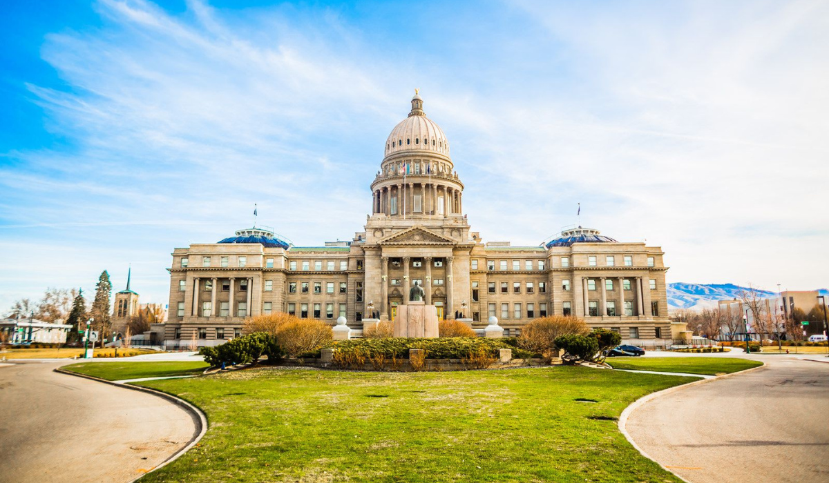 State capitol building with a central dome, viewed across a green lawn under a partly cloudy sky