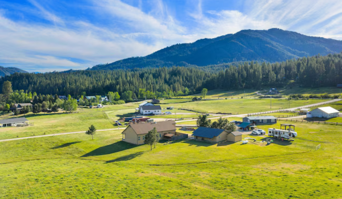 Scattered houses on a green valley plain with forested mountains under a blue sky