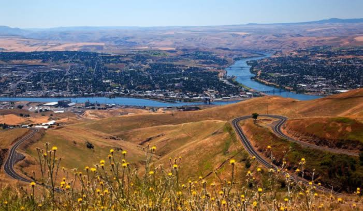 Panoramic river valley with a winding road, golden hills, and a city in the distance