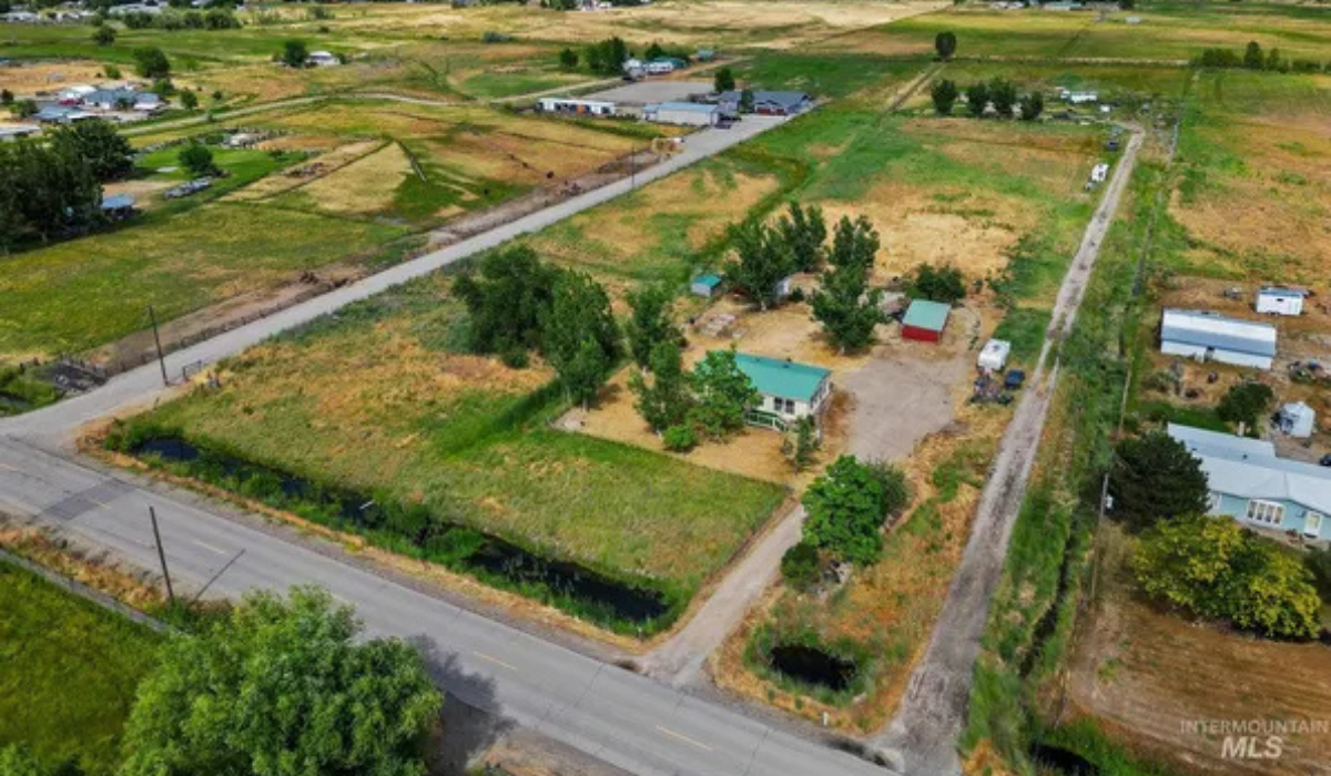 Aerial view of a rural neighborhood with roads, open fields, and scattered houses and trees.