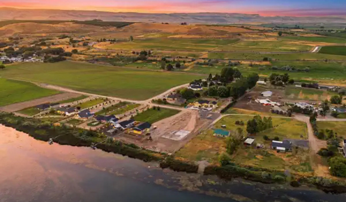 Aerial view of a rural lakeside village with fields, roads, and buildings at sunset.