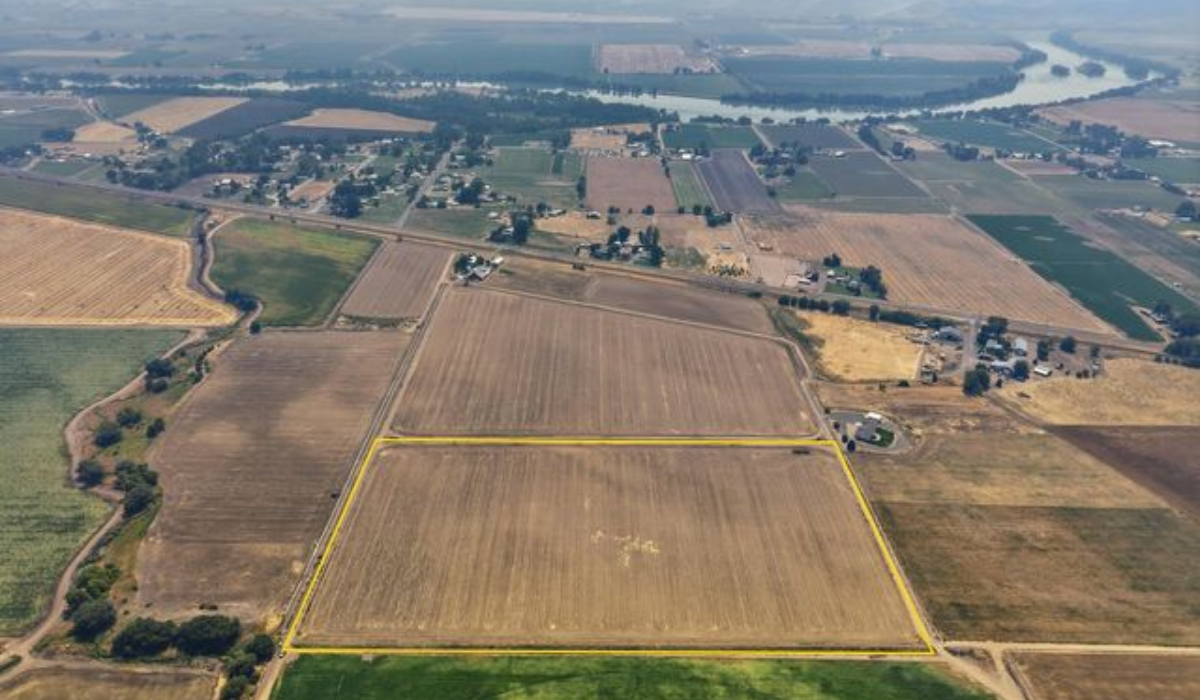 Aerial view of large farm fields with a yellow outlined plot and river winding in the distance