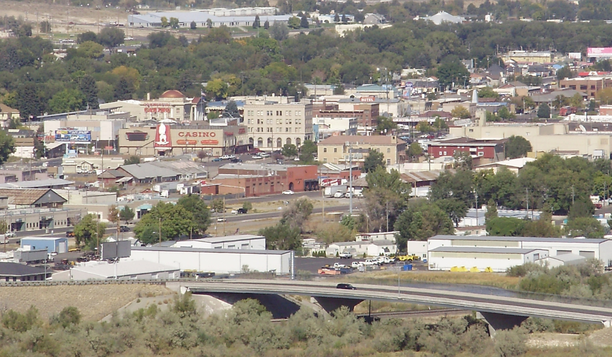 Wide cityscape with low buildings, roads, and trees under a hazy sky.