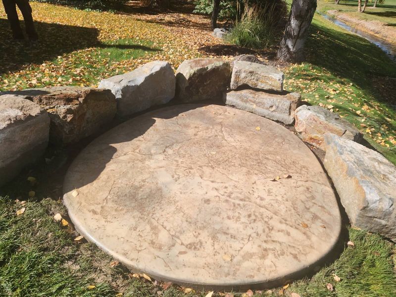 Stone outdoor fire pit surrounded by low rock seating in a grassy park area