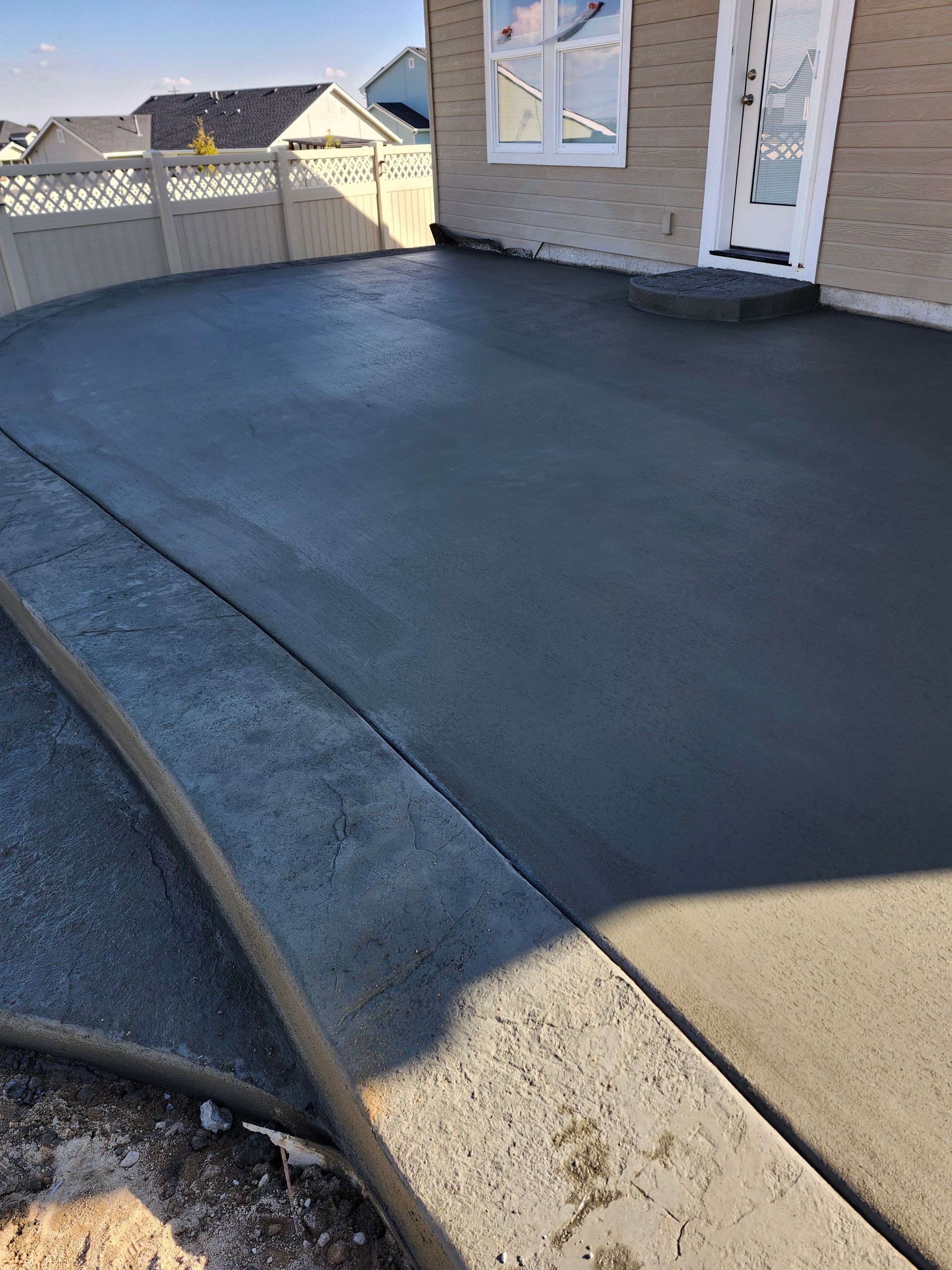 Freshly coated black concrete patio beside a house and white fence