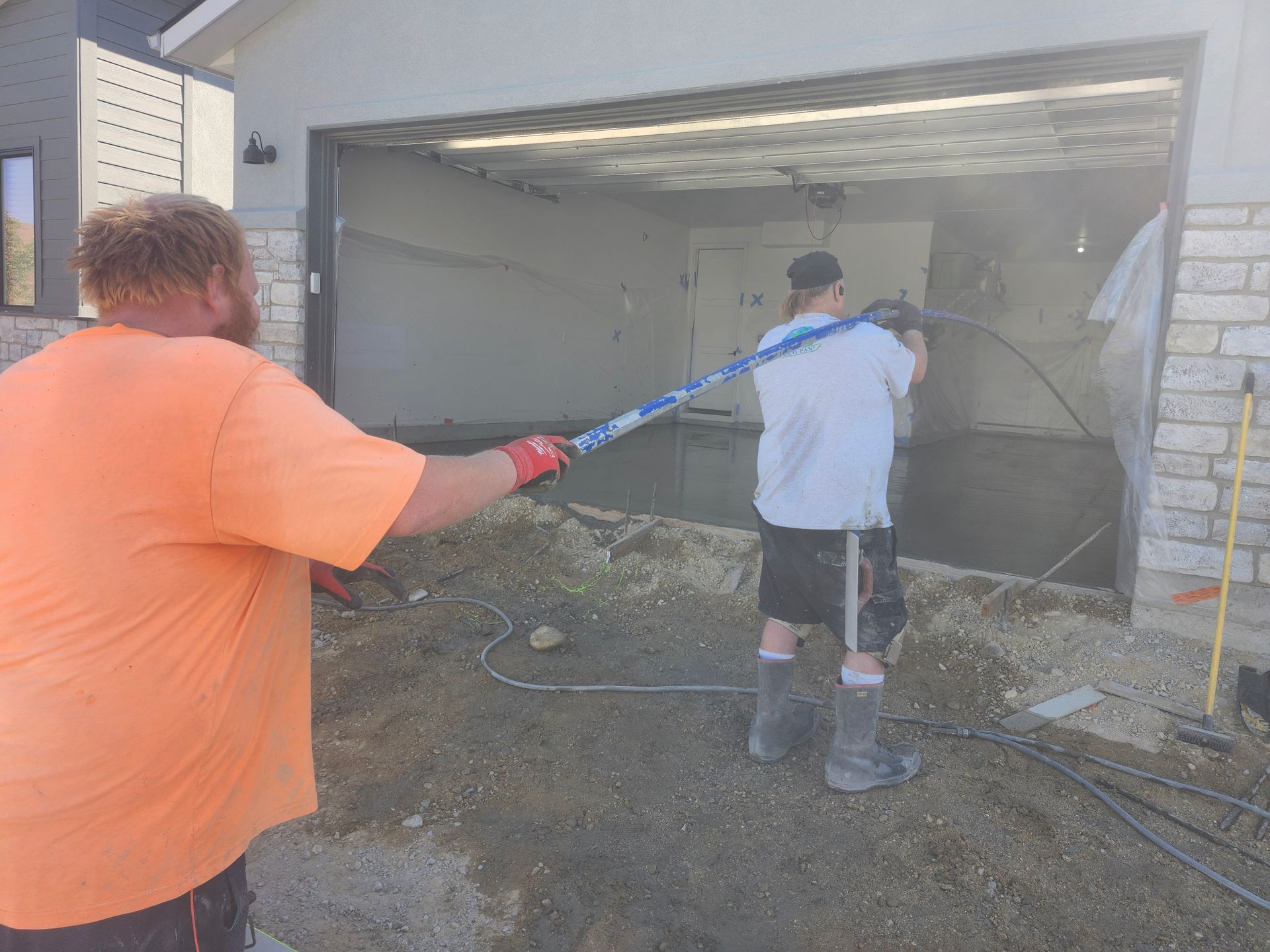 Two workers use a hose to spray debris out of a damaged garage.