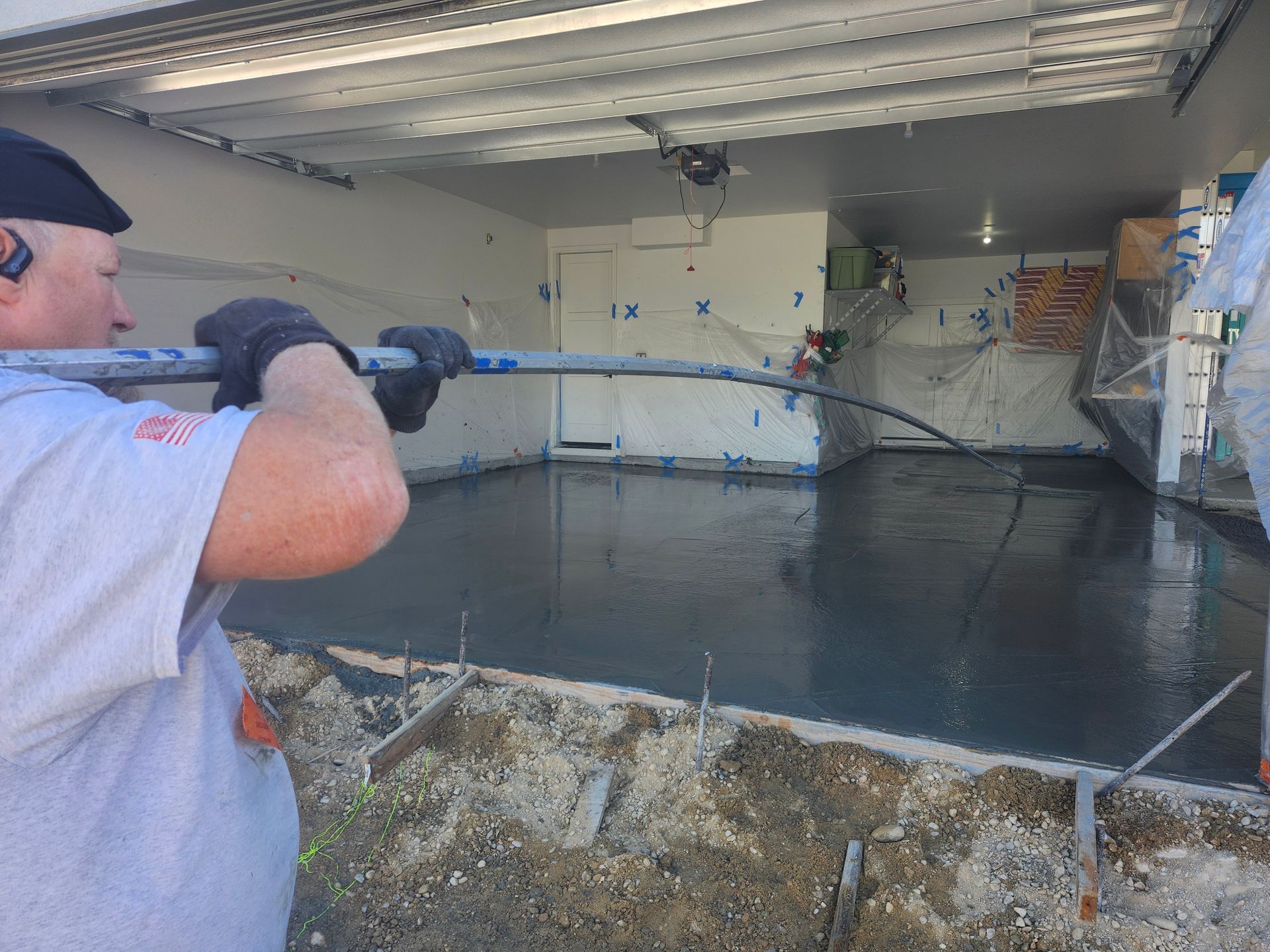 Worker pressure-washing a garage floor, spraying dark water inside a concrete bay