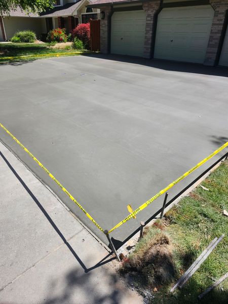 Fresh concrete driveway slab outlined with yellow tape beside a garage and curb