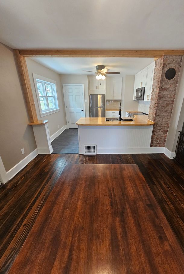 A living room with hardwood floors and a kitchen in the background.