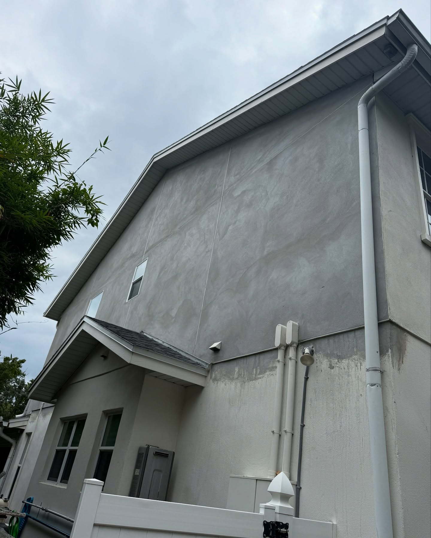 Exterior side wall of a two-story gray stucco house with a vertical seam and a lower section with two windows.