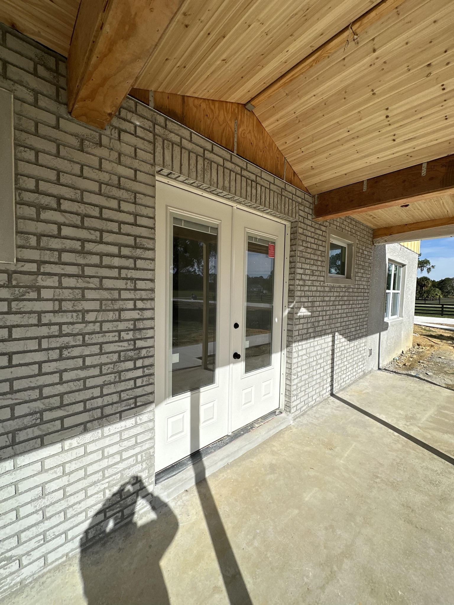 A covered brick porch with a set of white double glass doors leading into a building.