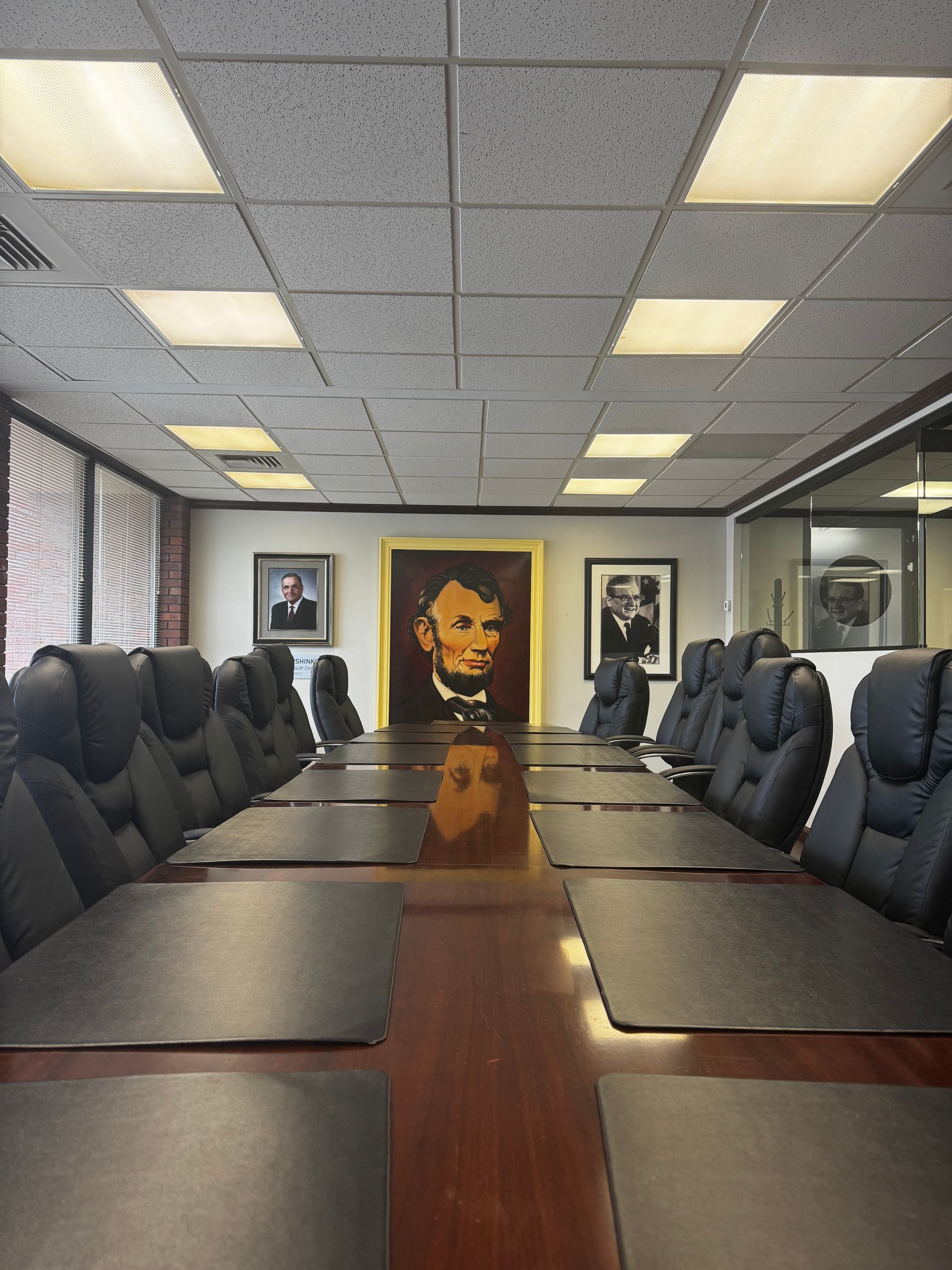 Empty conference room with long table, leather chairs, and portraits on the wall.