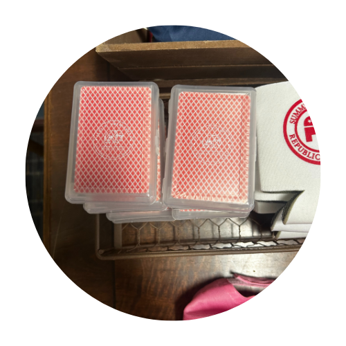 Two decks of playing cards in plastic cases on a wooden shelf, with a red and white logo on the right.