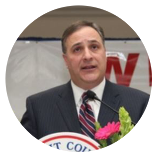 Man in suit speaking at a podium with a flower and a sign that says 