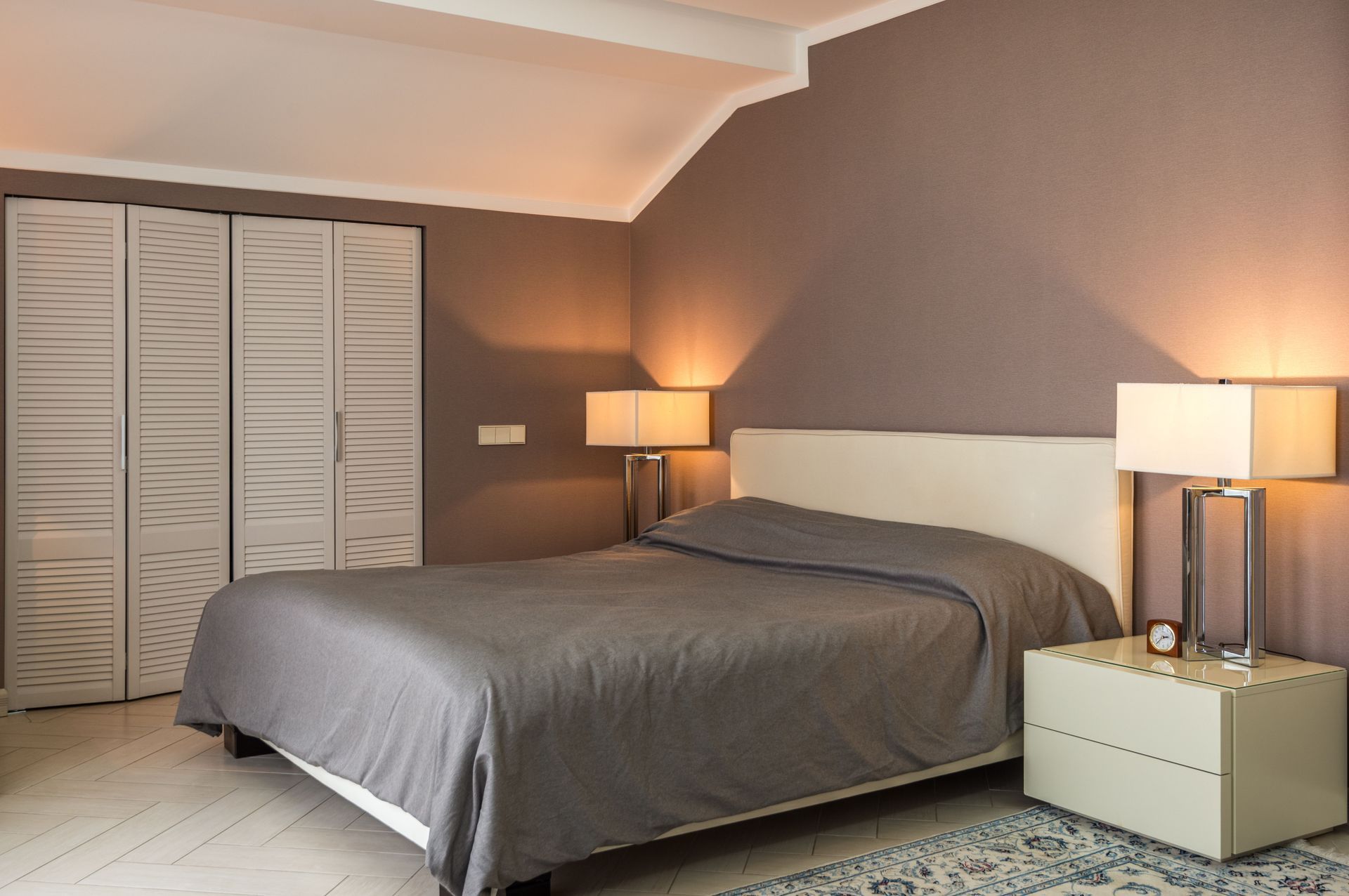 Cozy bedroom with gray bedspread, bedside lamps, and closet doors on the left