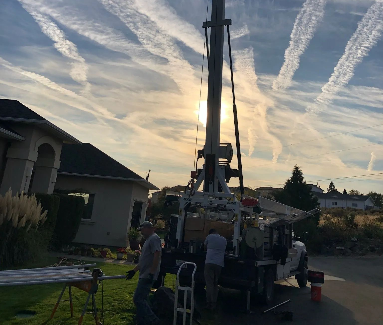 Workers gather around a utility truck with a raised boom at sunset in a suburban street.