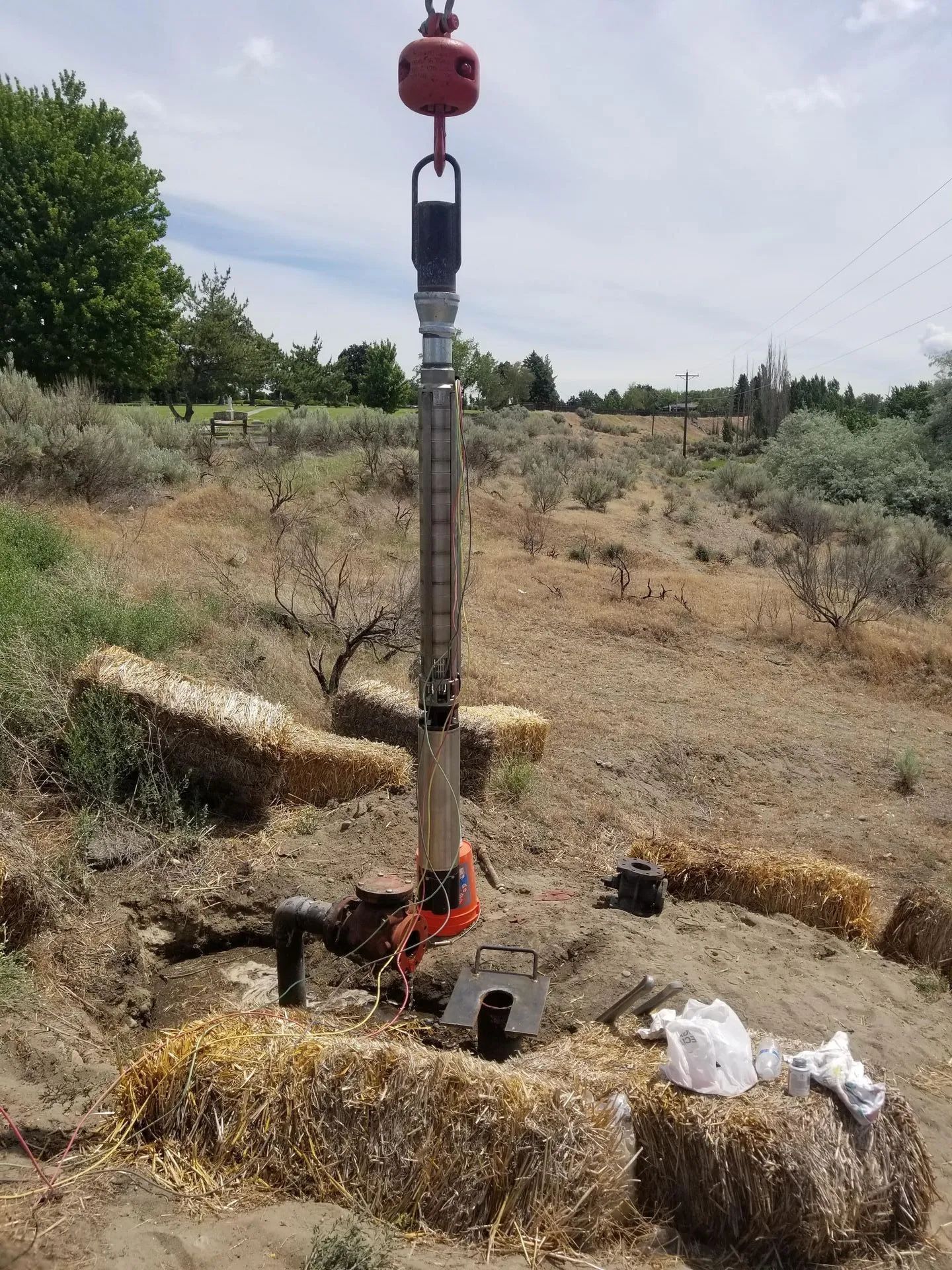 Well being installed in a dry, grassy field with a crane overhead.