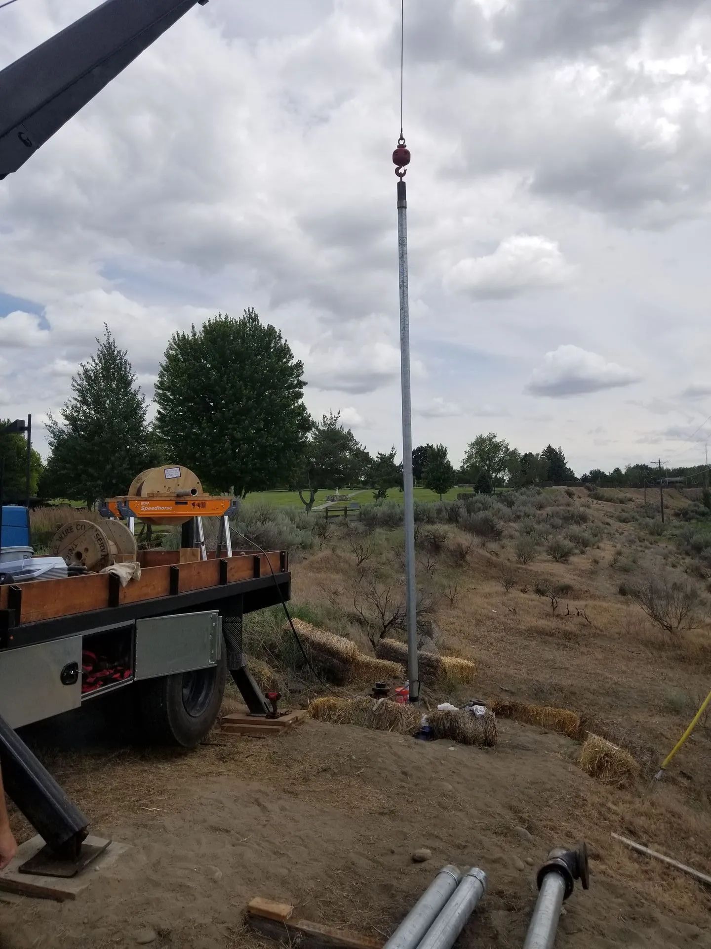 Crane lifting a tall metal pole at a dirt construction site beside a truck.