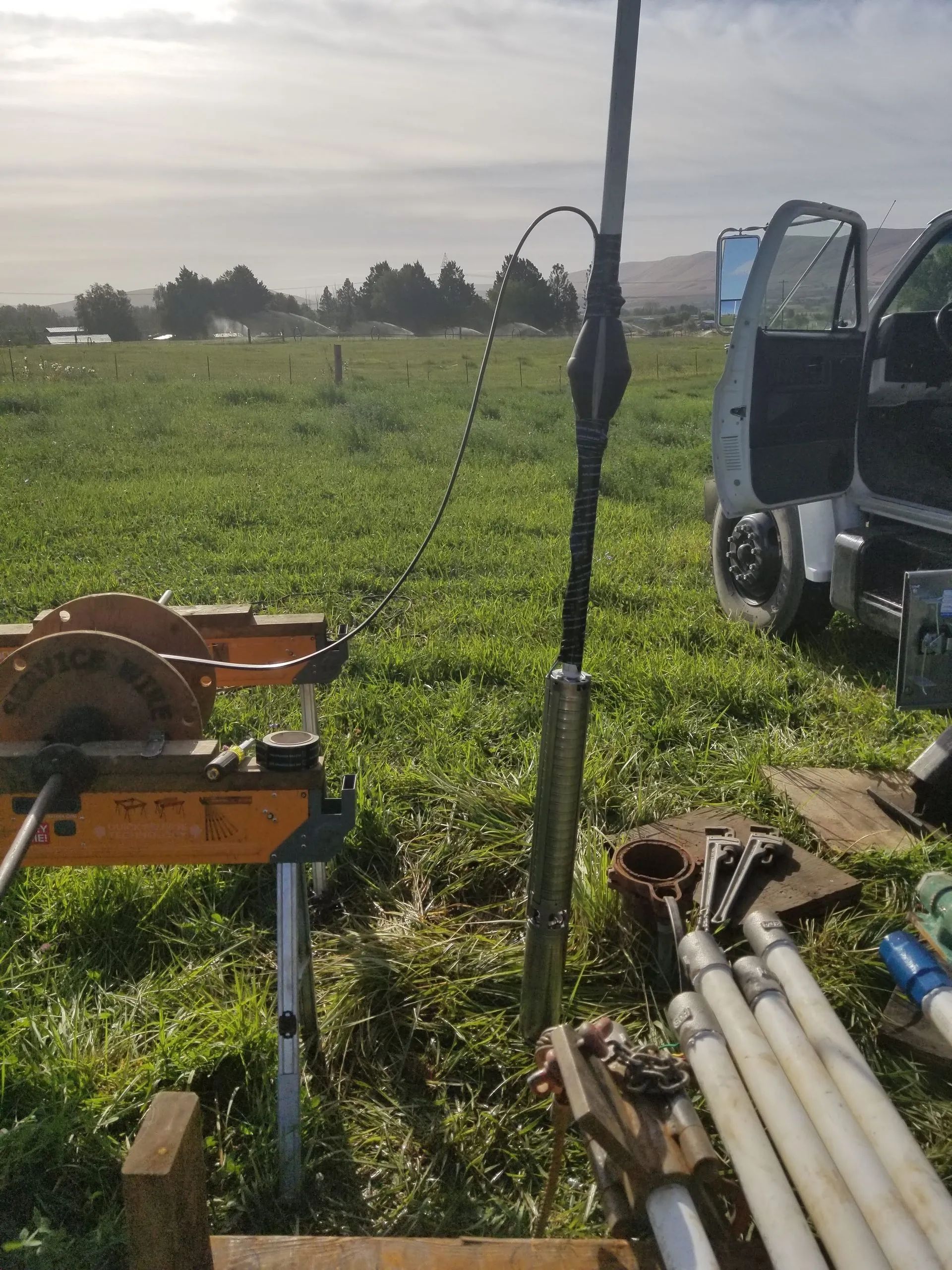 Farm field with equipment and pipes beside an open vehicle under a cloudy sky