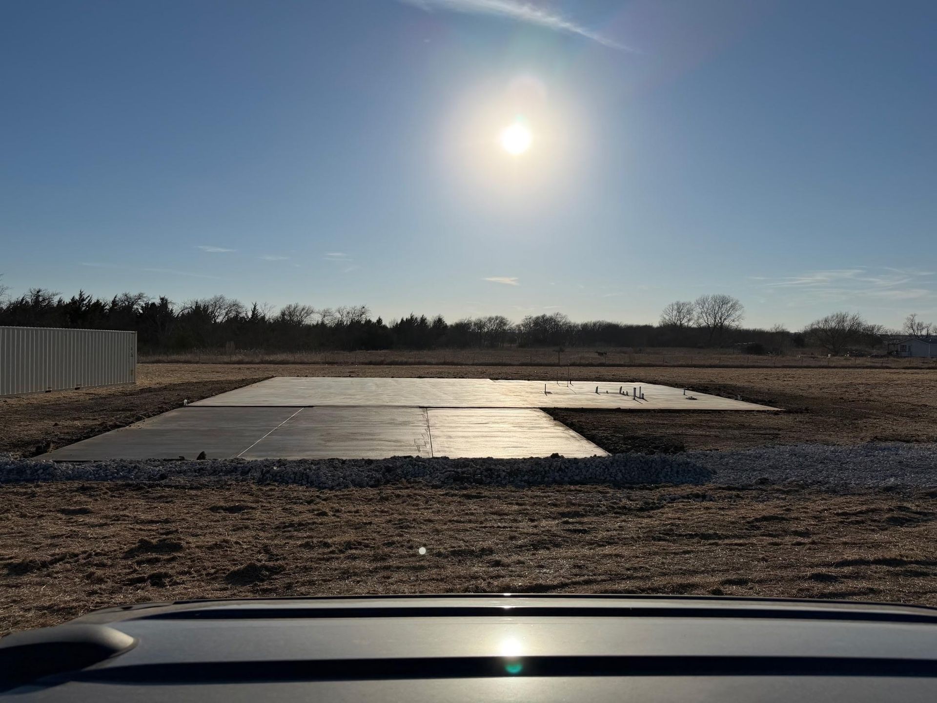 A concrete building slab sits in a field under a bright sun in a clear blue sky.
