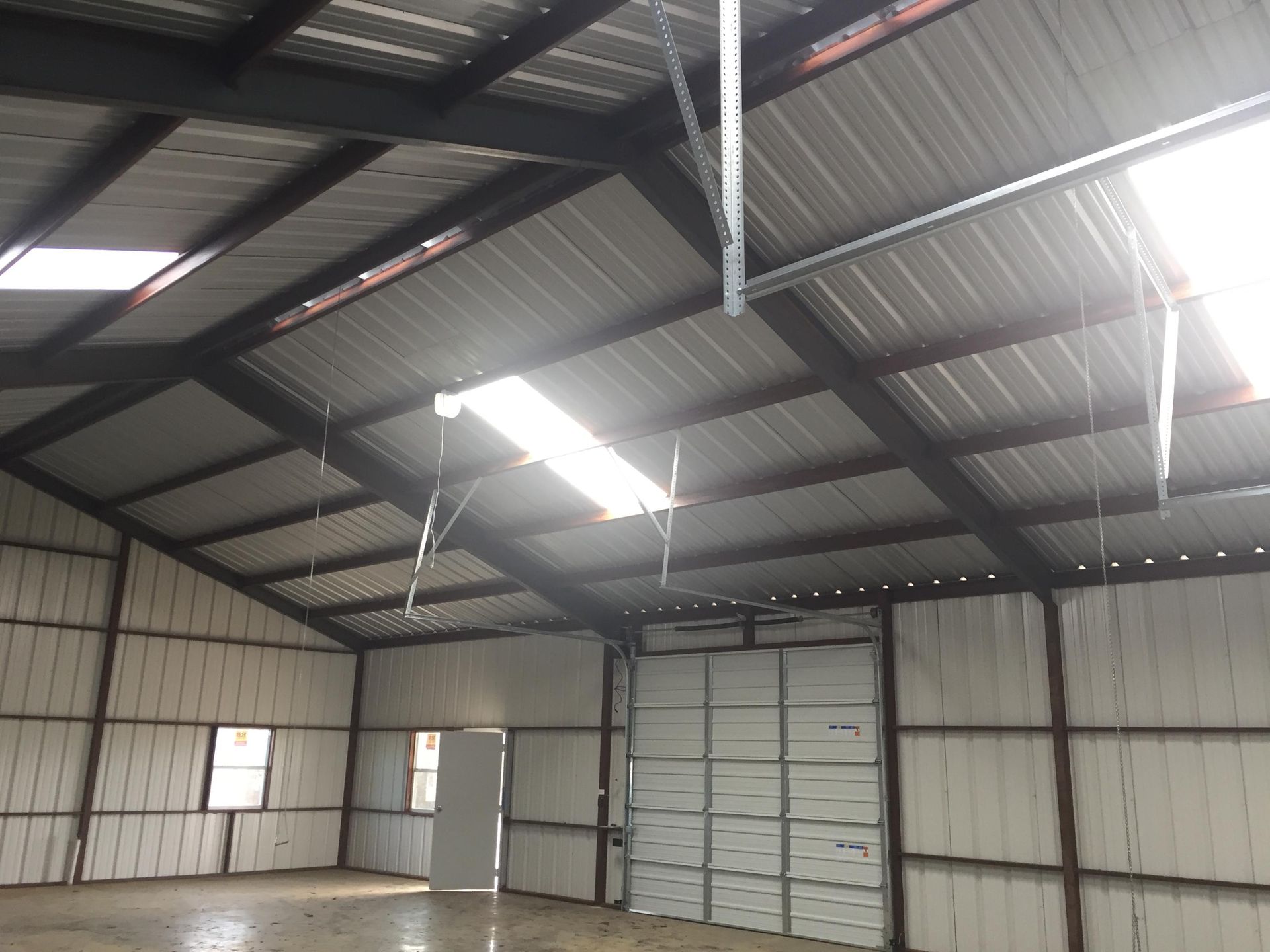 An interior view of a spacious warehouse with metal walls and a high-pitched ceiling featuring rectangular skylights.