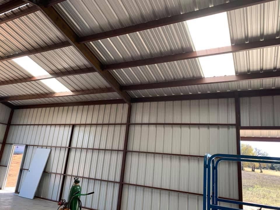 Interior of a metal building featuring white ribbed walls and a ceiling with skylight panels and exposed steel beams.