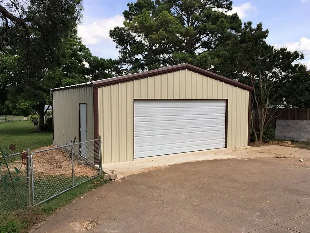 A detached metal garage with beige walls, a brown trim, a white roll-up door, and a single side entry door.